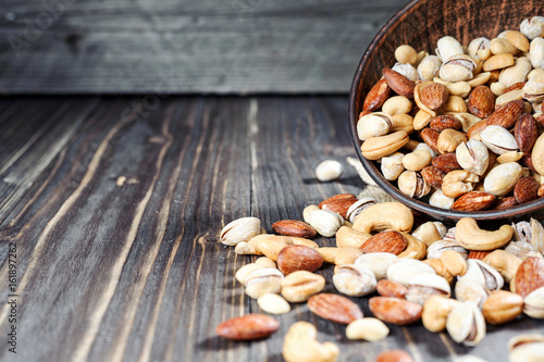Mixed nuts spilling out of bowl on wooden table. Macro still-life with shallow dof