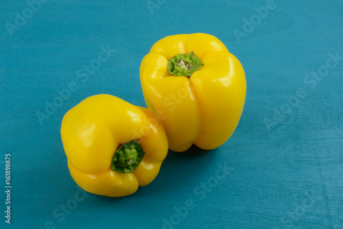 Two raw whole yellow bell peppers on blue wood background