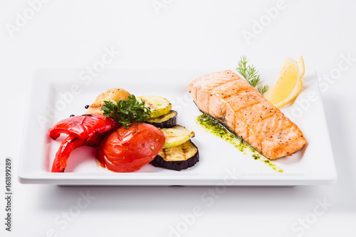 Healthy food, red fish, vegetables, herbs, lemon on a white plate and a white background