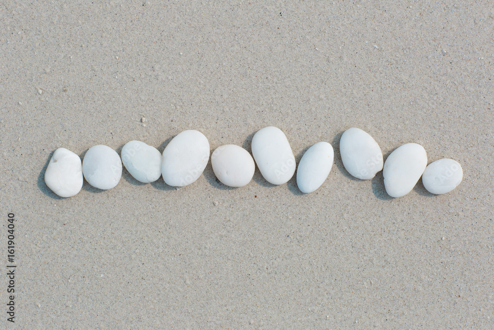 White pebbles, round small stones in a row on a wet white sand beach, space for letters or text White pebbles, round small stones in a row on a wet white sand beach, space for letters or text