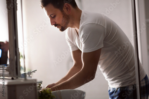 Handsome young man washing face in bathroom