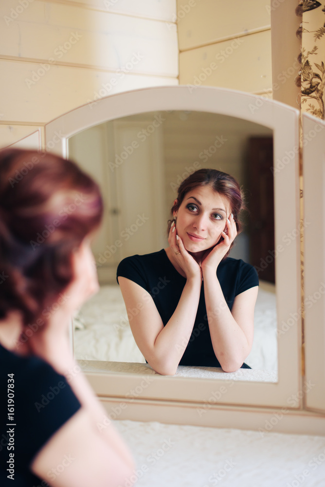 Beautiful young girl in a black dress sits in front of a vintage mirror, reflected in three mirrors Beautiful young girl in a black dress sits in front of a vintage mirror, reflected in three mirrors