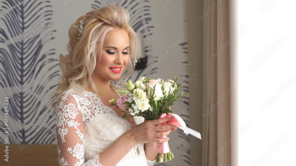 bride with wedding bouquet looks out the window and smiling at camera bride with wedding bouquet looks out the window and smiling at camera