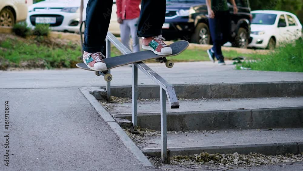 Close up shot of the skateboarder's legs, who performs a gliding on the board along the stair railings facing forward in summer time Close up shot of the skateboarder's legs, who performs a gliding on the board along the stair railings facing forward in summer time