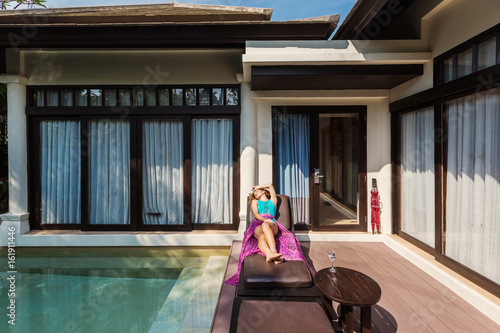 Woman lying on chaise lounge near pool luxury villa, have sunbathe, enjoying summer vacation