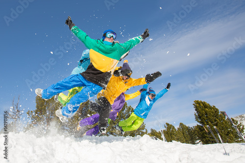Group of happy friends having fun jumping to snow. Ski and snowboard holiday
