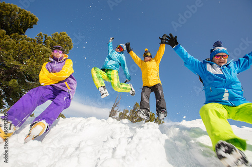 Group of happy friends having fun jumping to snow. Ski and snowboard holiday