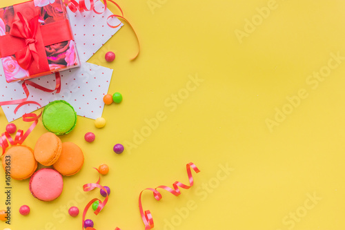 Birthday concept with wrapped gift and sweets on yellow background top view copyspace