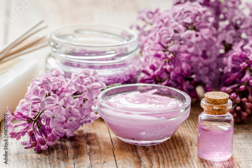 organic salt, cream, extract in lilac cosmetic set with flowers on wooden table background