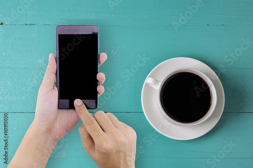 Man hand holding smart phone with white blank empty screen on blue desk table.