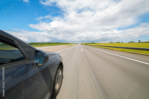 The car moves at great speed on highway at the sunny summer day.