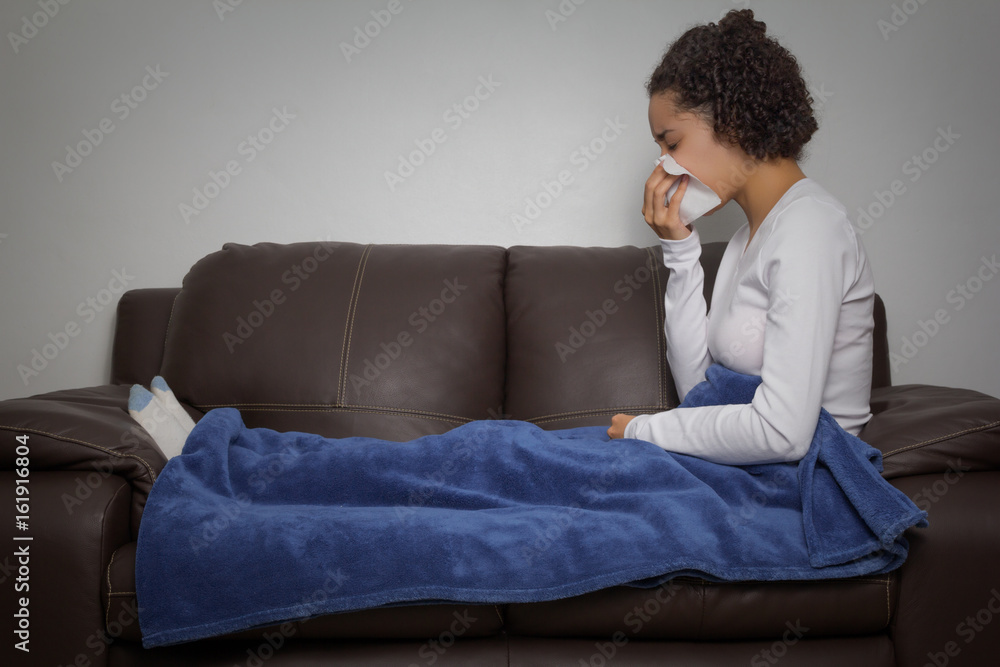 Woman is sneezing. Sitting on the couch.