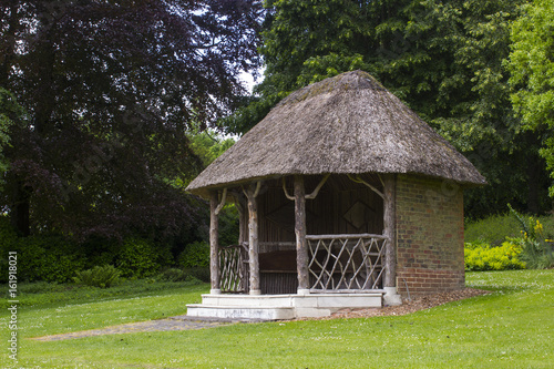 Thatched summer house surrounded by beautiful flower beds and gravel paths in the large gardens at West Dean gardens in Hampshire, England  © Michael