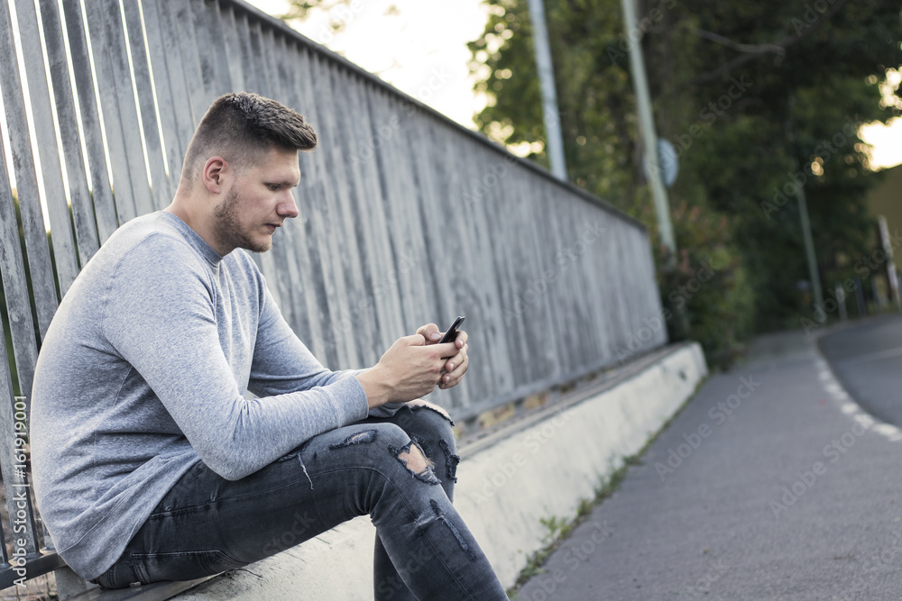 Obraz premium Junger Mann ist mit seinem Handy beschäftigt