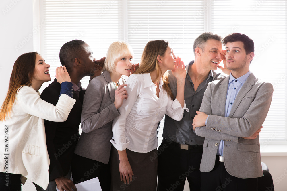 Secretive Business Colleagues Whispering In The Office Secretive Business Colleagues Whispering In The Office