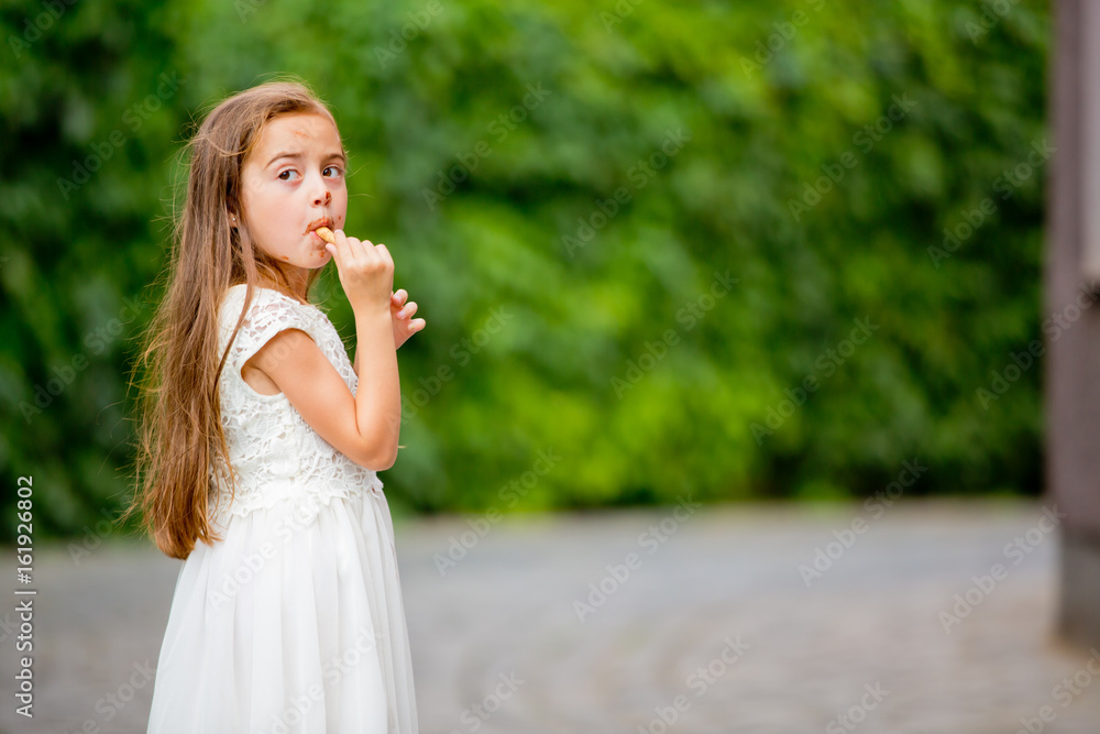 A little girl in a white dress is eating ice cream. A little girl in a white dress is eating ice cream.
