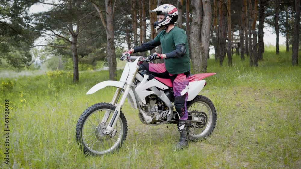 An adult man in a protective helmet and knuckles on his feet winds a mountain bike that stands in the woodland for riding An adult man in a protective helmet and knuckles on his feet winds a mountain bike that stands in the woodland for riding