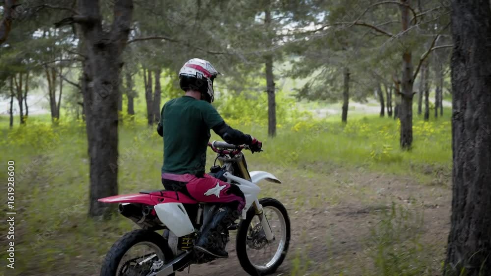 An athlete wearing a protective helmet and special uniform rides a cross-country motorcycle on a forest part in nature An athlete wearing a protective helmet and special uniform rides a cross-country motorcycle on a forest part in nature