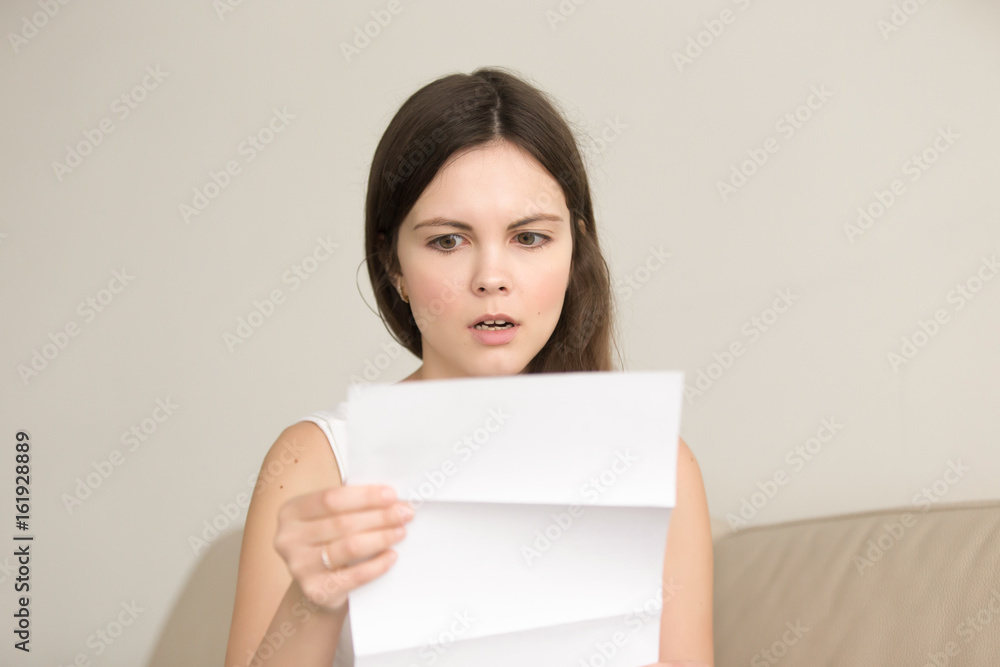 Surprised young woman reading letter with bad news. Worried attractive lady looking on document with unexpected written notice, shocked with bills, tax form or wrong payment. Message about loan debt Surprised young woman reading letter with bad news. Worried attractive lady looking on document with unexpected written notice, shocked with bills, tax form or wrong payment. Message about loan debt