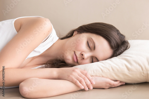 Cute young woman sleeping on side on soft pillow on sofa, lying relaxed with closed eyes. Tired beautiful lady resting at home, enjoying pleasant leisure. Daytime drowsiness and nap concept. Close up