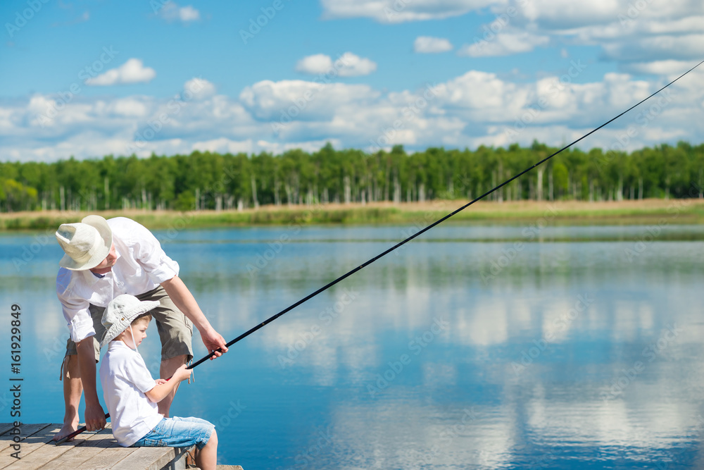 The father teaches his son, to fish on the river from the pier The father teaches his son, to fish on the river from the pier