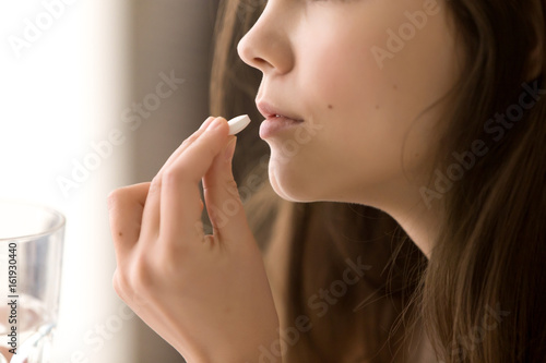 Bild auf Leinwand Close up image of woman putting white round pill in mouth