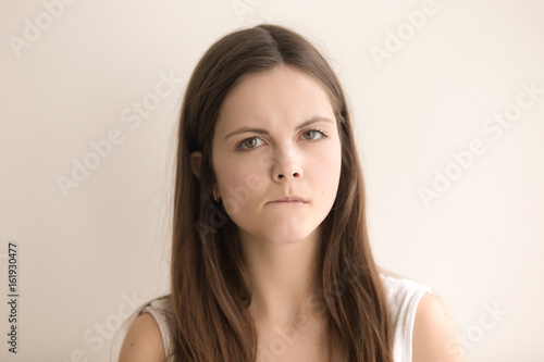 Headshot portrait of nervous confused young woman. Worried teenager girl biting lip and looking at camera with sadness, doubts in decision. Stressed female thinking about problem. Close up. Front view