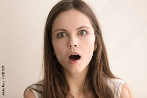 Headshot portrait of puzzled young woman. Attractive teen girl with confused facial expression looking at camera with surprise. Pretty female feels suddenly shocked or worried. Close up. Front view