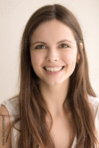 Headshot portrait of happy young woman. Charming teen girl with joyful facial expression looking at camera with beautiful smile. Pretty lady feeling enthusiasm and admiration. Close up. Front view