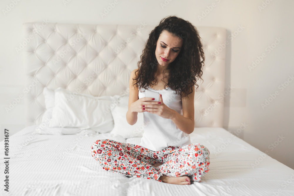 Beautiful woman using phone while sitting on bed Beautiful woman using phone while sitting on bed