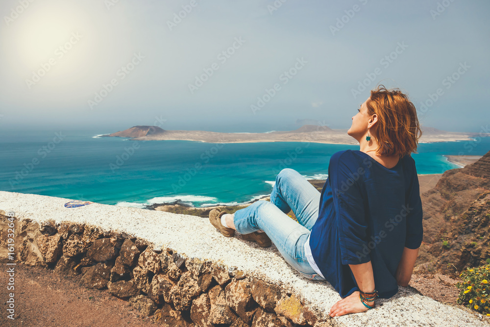 Young woman sitting on stone fence looking at sea
