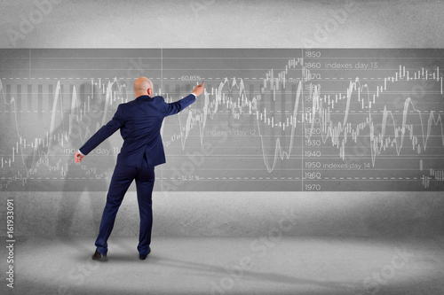 Man in front of a wall writing on a stock exchange interface - tradex concept