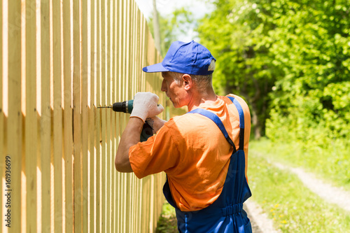 Close up portrait of skilled worker building wooden fence with cordless electric screwdriver
