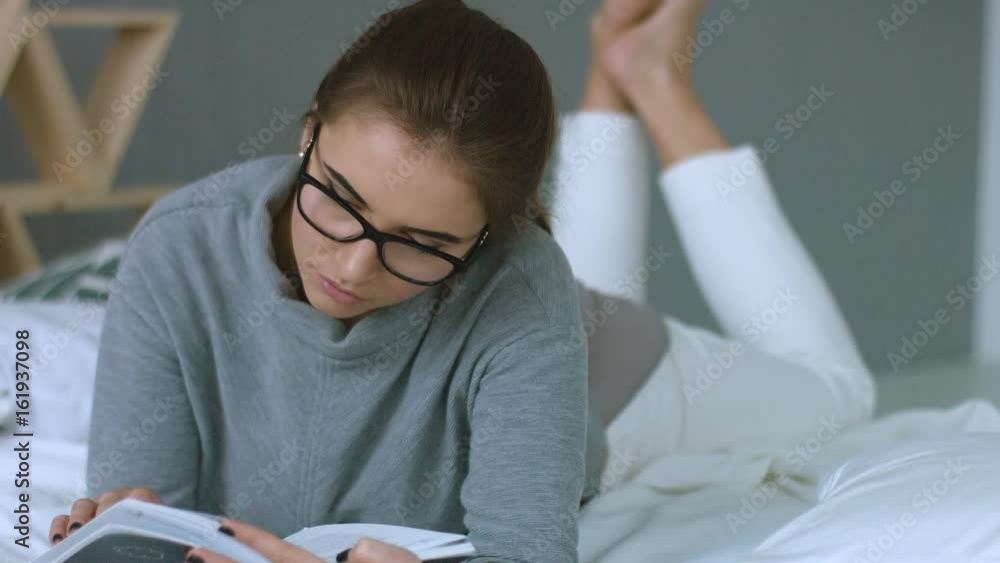 Young woman with glasses reading book while lying on the bad. Young woman with glasses reading book while lying on the bad.