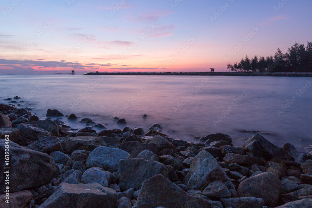 Landscape view of stone ridge coast, sea and lighthouse in the beautiful morning pink blue sky, background
