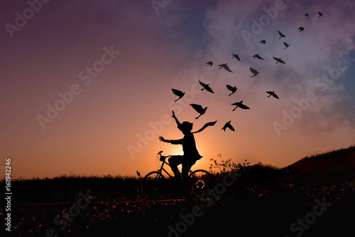 Freedom concept, Silhouette of happy person raised arms on bicycle in natural scene, Birds fly on beautiful sunrise or sunset sky