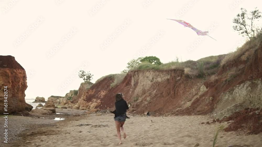 Young hipster woman releasing colorful kite on the beach in the evening. Slowmotion shot