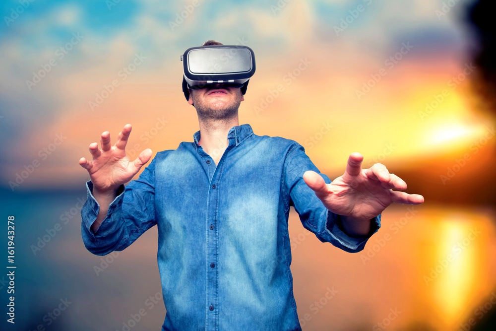 Closeup of bearded young man wearing virtual reality goggles. Smartphone using with VR headset. Horizontal, blurred. Sunset background Closeup of bearded young man wearing virtual reality goggles. Smartphone using with VR headset. Horizontal, blurred. Sunset background