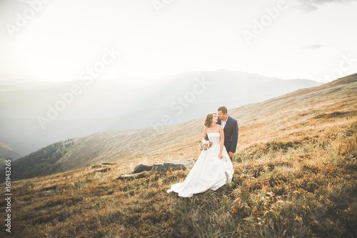 Beautiful wedding couple posing on top of a mountain at sunset