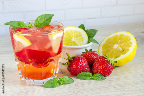 A refreshing summer drink with ice, strawberries and lemon on a wooden background. The concept of fruit drink.