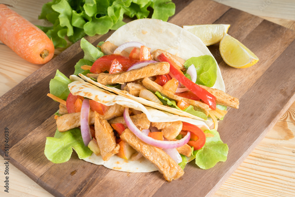 Obraz premium Grilled meat with onion and bell peppers, tomato,lettuce and serve with flour tortilla on wooden board.