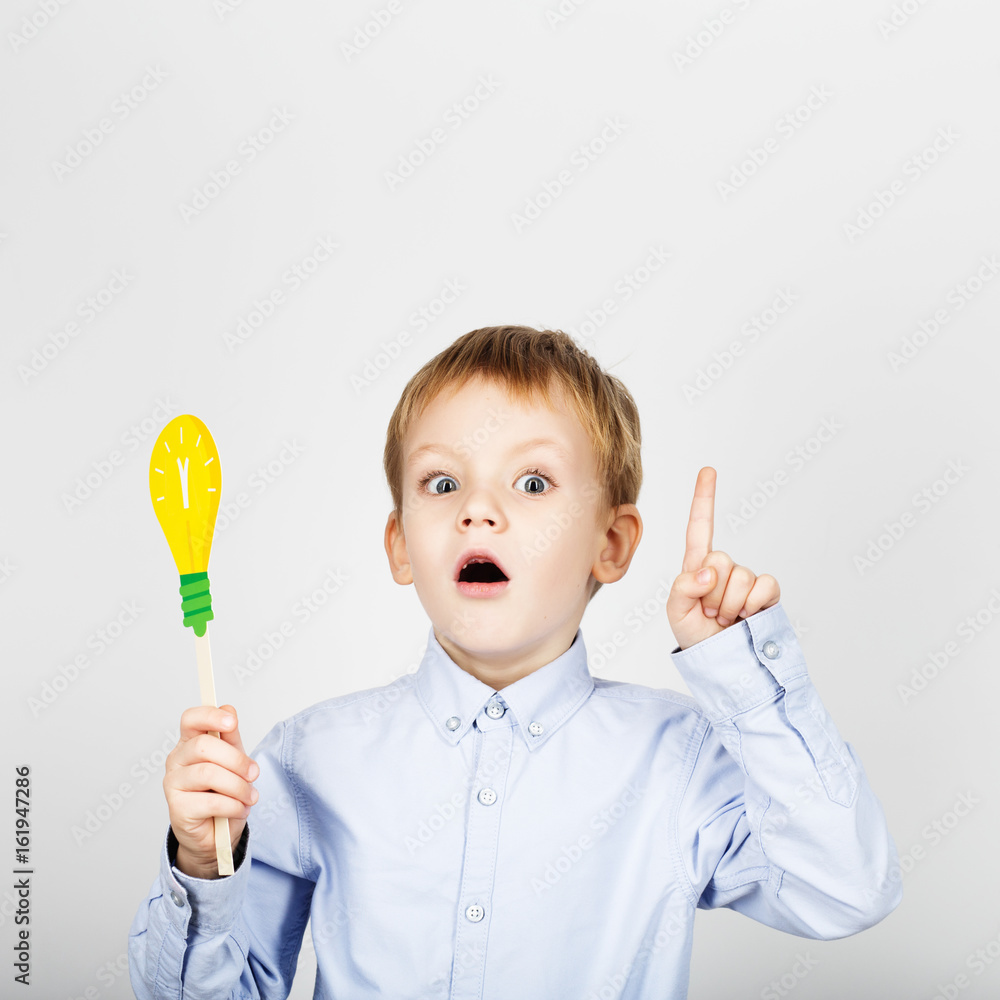 Cute boy with yellow paper lightbulb against a white background. little student gesturing thumb holding toy bulb. Cheerful smiling Kid with funny photo props. School concept. Cute boy with yellow paper lightbulb against a white background. little student gesturing thumb holding toy bulb. Cheerful smiling Kid with funny photo props. School concept.