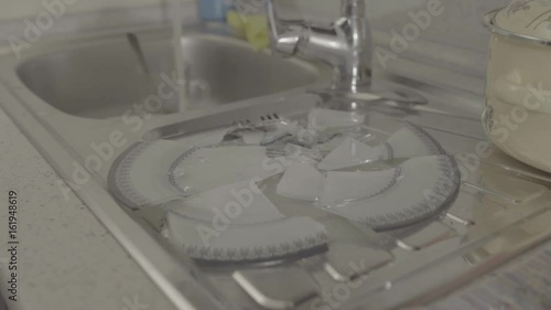 A broken dish is on the kitchen, water flows from the tap photo