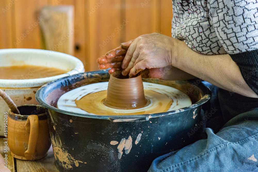 An elderly woman decorates a clay bowl on a potter's wheel
