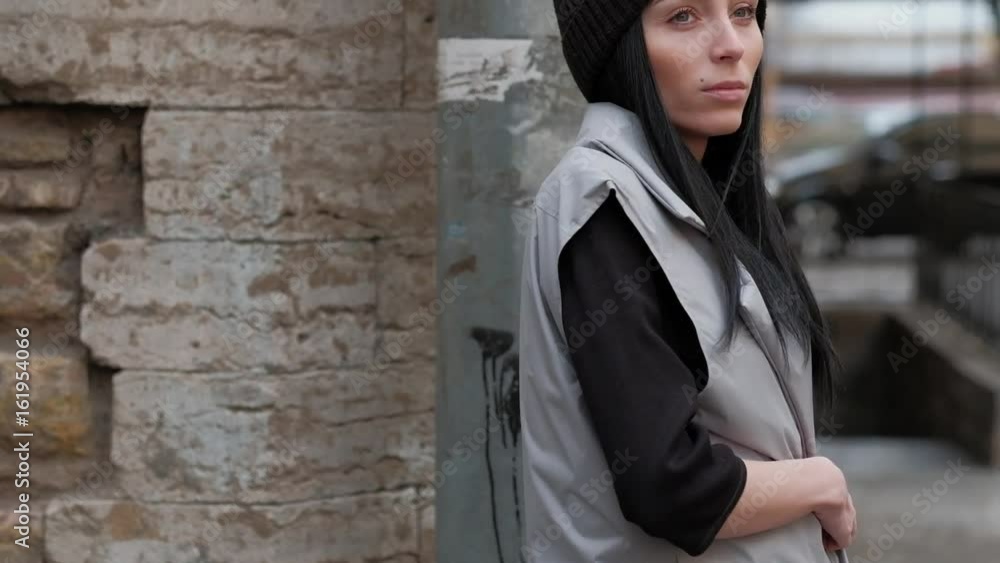 Stylish Fashion Girl, With Long Black Hair, Walking in the Street, on Background Brick Wall, in Grey Cloak and Black Hat Stylish Fashion Girl, With Long Black Hair, Walking in the Street, on Background Brick Wall, in Grey Cloak and Black Hat