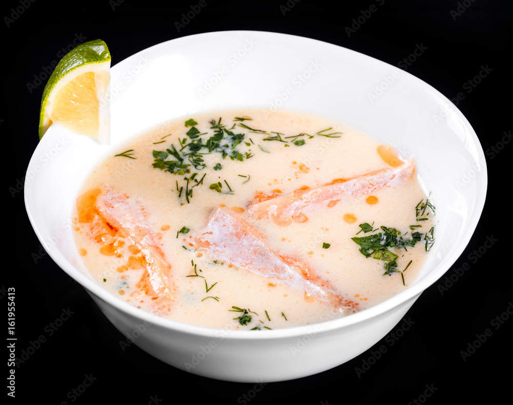 Fish soup with salmon and shrimps, dill, potatoes, lemon and vegetables in bowl, isolated on black background, healthy food. Top view