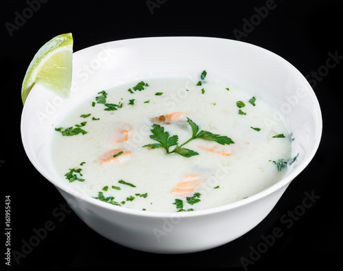 Fish soup with salmon and shrimps, parsley and lemon in bowl, isolated on black background, healthy food. Top view