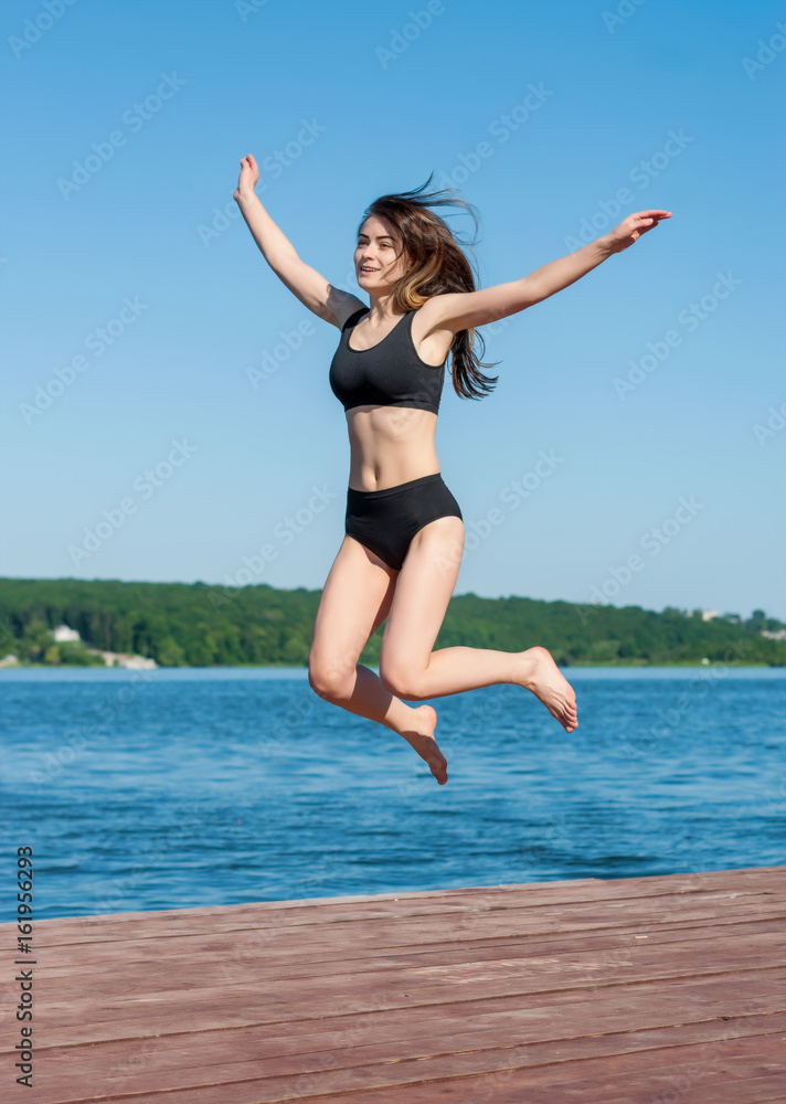 Fitness girl jumping on the shore of Lake