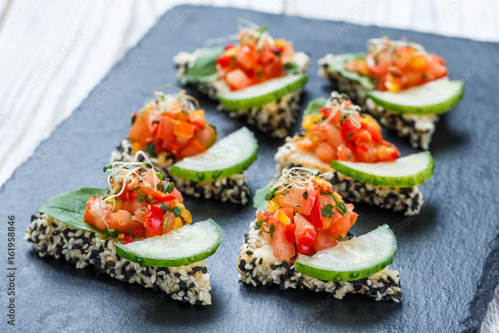 Appetizer canape with chopped vegetables and sesame on stone slate background close up. Delicious snacks, sandwiches, crostini, bruschetta, antipasti on party or picnic time. Top view Appetizer canape with chopped vegetables and sesame on stone slate background close up. Delicious snacks, sandwiches, crostini, bruschetta, antipasti on party or picnic time. Top view