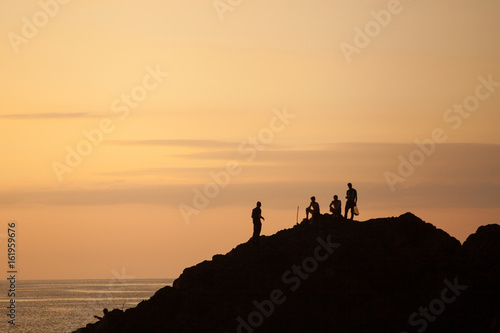 Silhouettes of people on the mountain towering above the sea at night